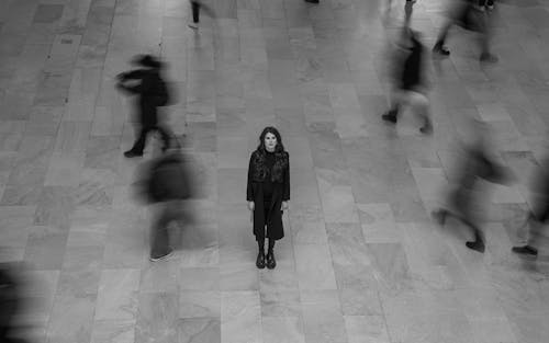 A black and white image of a woman standing alone whilst blurred people move around her